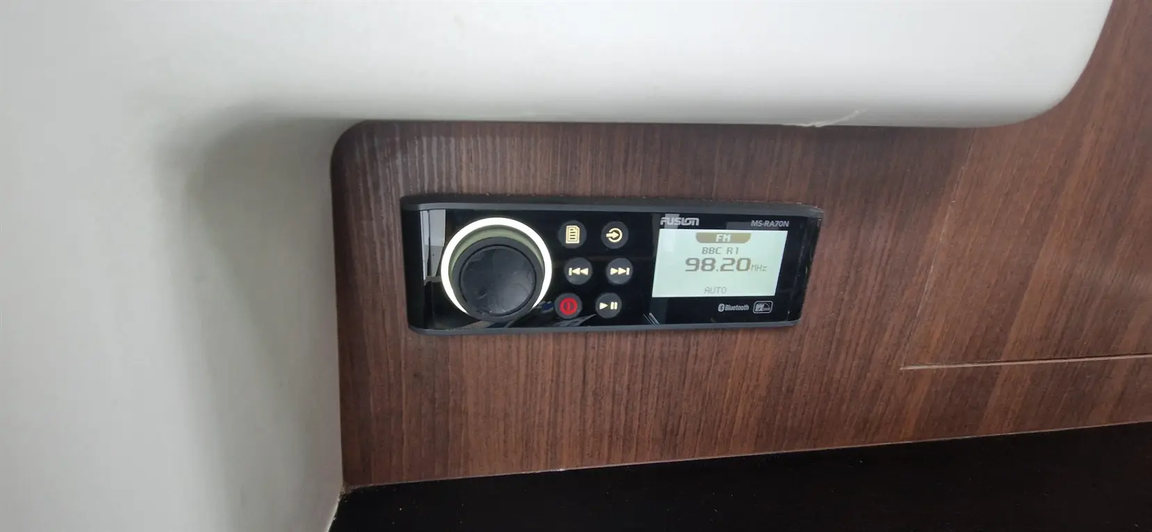 Fusion MS-RA70N marine stereo display showing FM, tuned to BBC R1 at 98.20 MHz, with various control buttons below.